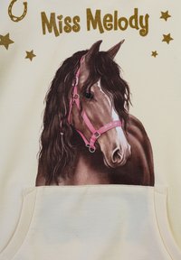 Felpa di colore crema chiaro con un cavallo marrone dalla lunga criniera nera, che indossa una briglia rosa, circondato da stelle dorate e il testo "Miss Melody."