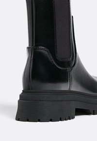 Svart läderankelboots med en slät yta, elastisk sidopanel och en texturerad gummisula med spår för grepp.