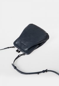 Navy nahka ristiolkalaukku, jossa on pehmeä, pyöreä muoto. Varustettu yläklipsillä, säädettävällä hihnalla ja hienovaraisella kohokuvioidulla brändäyksellä edessä.
