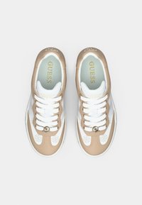 Sneakers marroni chiaro e bianche con accenti traforati, pelle strutturata, lacci rotondi e dettaglio del logo dorato sulla linguetta.