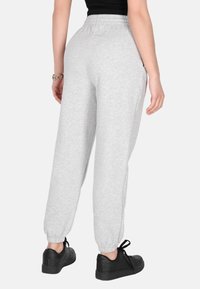 Grå joggingbukser med elastisk talje, smalle manchetter og sidelommer. Båret med sorte sneakers. Glat tekstur.