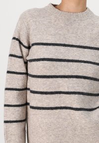 Beige knit sweater with black horizontal stripes. Crew neckline, ribbed hem, and soft texture. Casual fit with long sleeves.