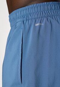 Shorts de sport bleu clair en tissu lisse et évacuant l'humidité. Dotés d'une taille élastique et de poches latérales avec une impression "DRYCELL".