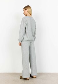 Szürke pamut pulóver hosszú ujjakkal és bordázott mandzsettával, széles szárú nadrággal párosítva. Simább textúra és laza fazon.