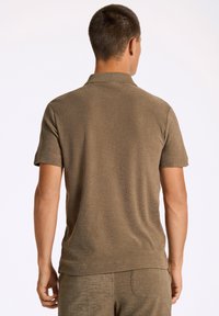 Khaki kortärmad polo skjorta med en texturerad, mjuk yta och en klassisk krage. Sitter tajt med en ren, enkel bakvy.