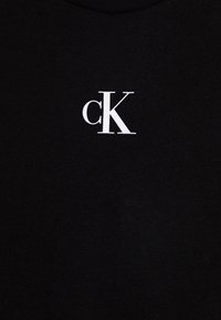 Czarna bawełniana koszulka z białym logo "cK" na piersi. Materiał wydaje się miękki, o gładkiej fakturze, z klasycznym okrągłym dekoltem.