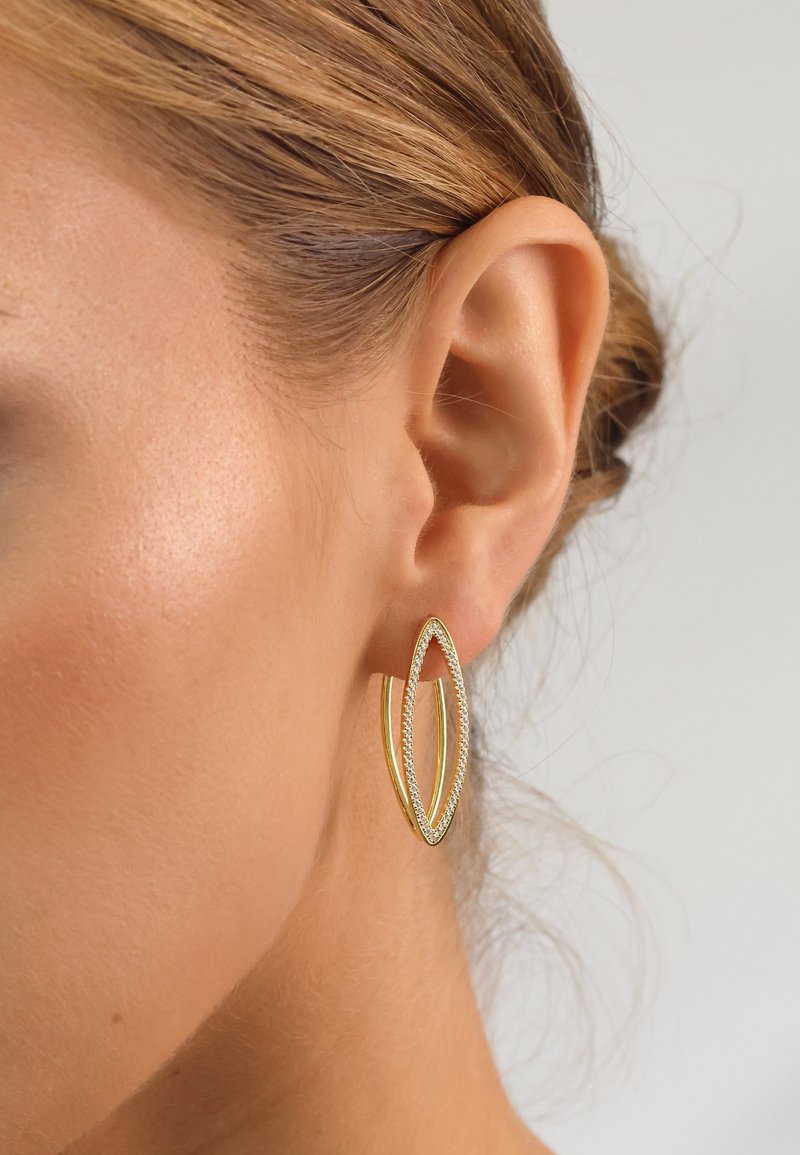 Goldfarbene Creolen mit ovaler Form, verziert mit kleinen klaren Steinen entlang des Randes, die eine glatte metallische Oberfläche präsentieren.