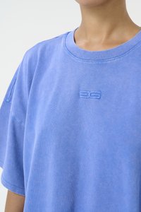 Blå bomulls t-skjorte med korte ermer, med rund hals og en liten brodert logo i midten. Myk tekstur.