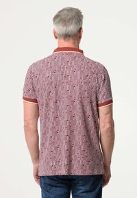 Rood-wit gestreepte polo-shirt met een gestructureerd oppervlak, geribbelde kraag en oranje accenten. Draagt met blauwe denim jeans.