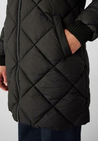Cappotto imbottito nero con chiusura a zip, caratterizzato da un motivo a rombi, polsini in maglia a coste e tasche laterali.