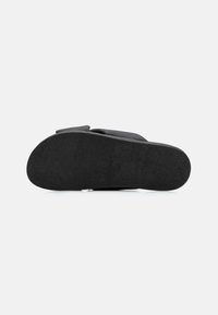Semelle de sandale noire avec une surface texturée, de forme légèrement arrondie, au design plat et avec un minimum de détails. Convient pour un usage décontracté.
