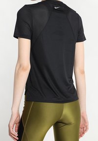 Musta lyhythihainen urheilu paita, jossa on verkkopaneelit, ja takana pieni logo sekä rento leikkaus. Rakennettu hengittävästä teksturoidusta kankaasta.