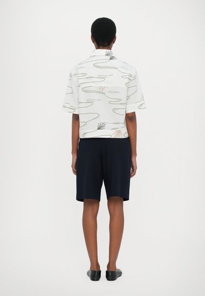 Short-sleeved white shirt with abstract green and beige patterns, paired with dark navy shorts and black slip-on shoes.