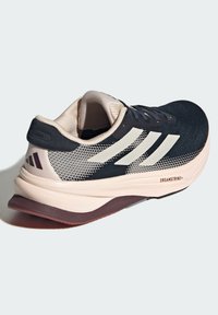 Scarpa sportiva nera e crema con tomaia in rete, tre strisce bianche, suola ammortizzata e suola in gomma con un leggero rialzo del tacco.