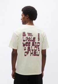 Μπεζ βαμβακερό t-shirt με κοντά μανίκια, με έγχρωμο γραφικό κείμενο στην πλάτη σε πράσινο και ροζ.