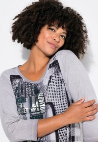 Un haut gris à manches longues présentant un design imprimé avec du texte et des motifs en noir et vert, fabriqué en tissu doux et léger.