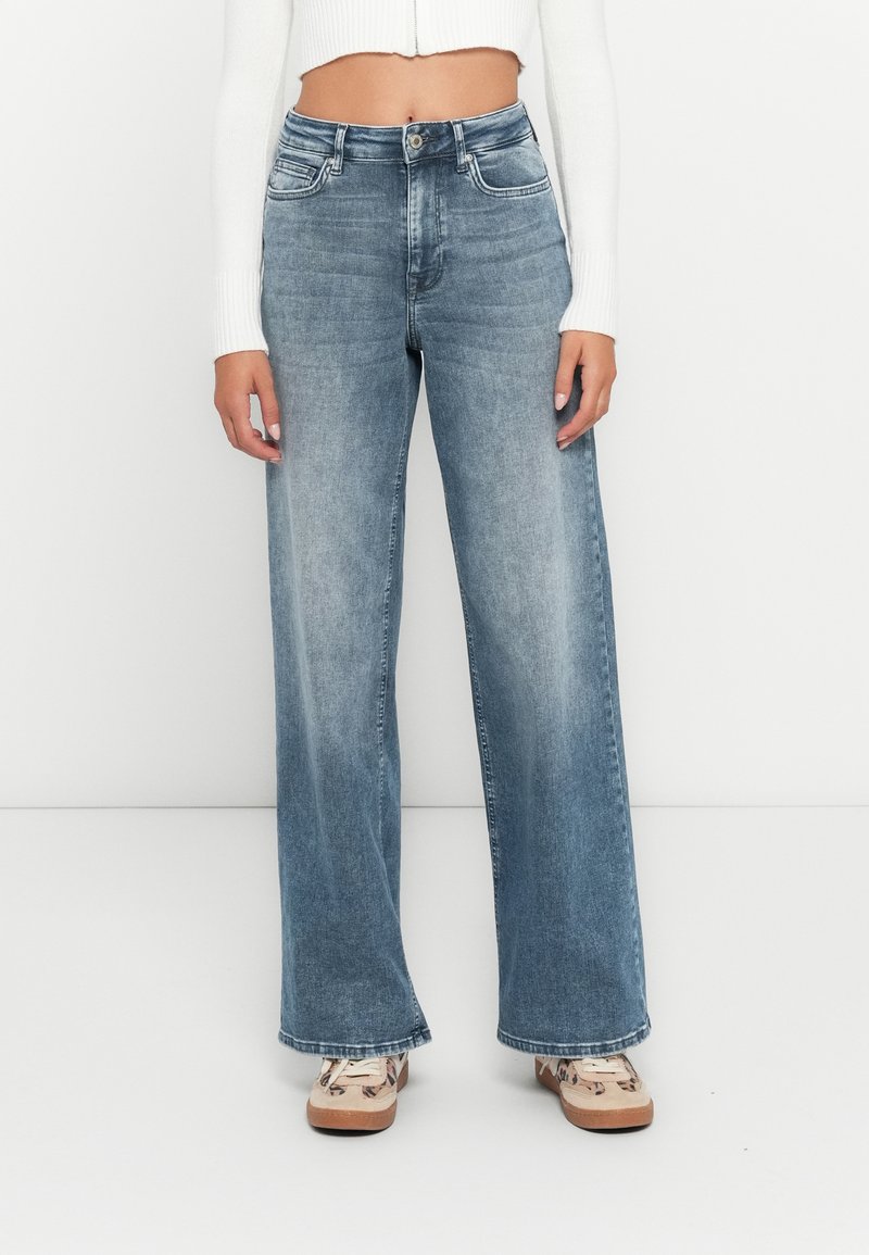 Jeans in denim a gamba larga con un lavaggio azzurro chiaro, dotati di vita alta, leggeri sbiadimenti e tasche anteriori. Tessuto liscio con cuciture a vista.