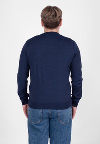 Granatowa dzianinowa bluza z długimi rękawami i okrągłym dekoltem, zestawiona z jasnoniebieskimi dżinsami. Gładka tekstura i dopasowany krój.