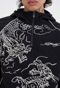 Giacca nera con cappuccio caratterizzata da ricami di drago bianco e motivi a nuvola, con design a mezza zip e logo del marchio sul petto. Texture morbida.