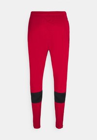 Pantalones deportivos rojos con un diseño ajustado, con acentos de malla negra en la parte inferior de las piernas, cinturilla elástica y textura de tela suave.
