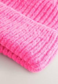 Pink knitted beanie with a textured ribbed pattern. Soft, fuzzy material with a thick cuff at the bottom, providing warmth and comfort.