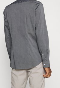 Grijze langetermijnshirt met een gladde textuur, voorzien van een contrasterende zwarte kraag, een shirtstaartzoom en witte knoopaccenten.