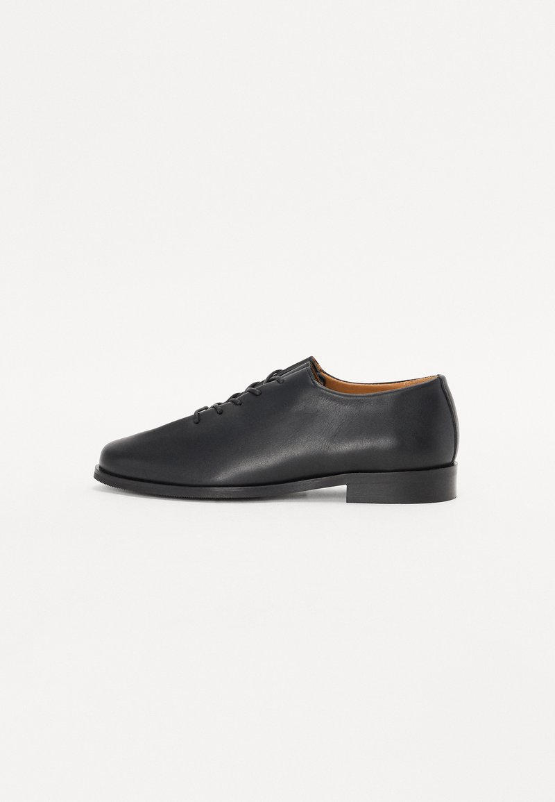 Black leather shoe with a smooth texture, rounded toe, six eyelets, and a low heel. The interior is brown leather. Simple design.