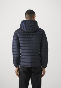 Navy blue padded jacket with a hood, featuring a quilted design and elastic cuffs, worn over dark jeans, viewed from the back.