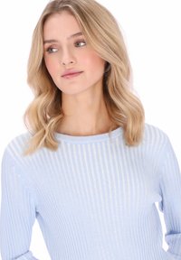 Világoskék bordázott pulóver lekerekített nyakkivágással. Finom fényes részletekkel és hosszú ujjakkal, melyek kiemelik a puha textúrát.