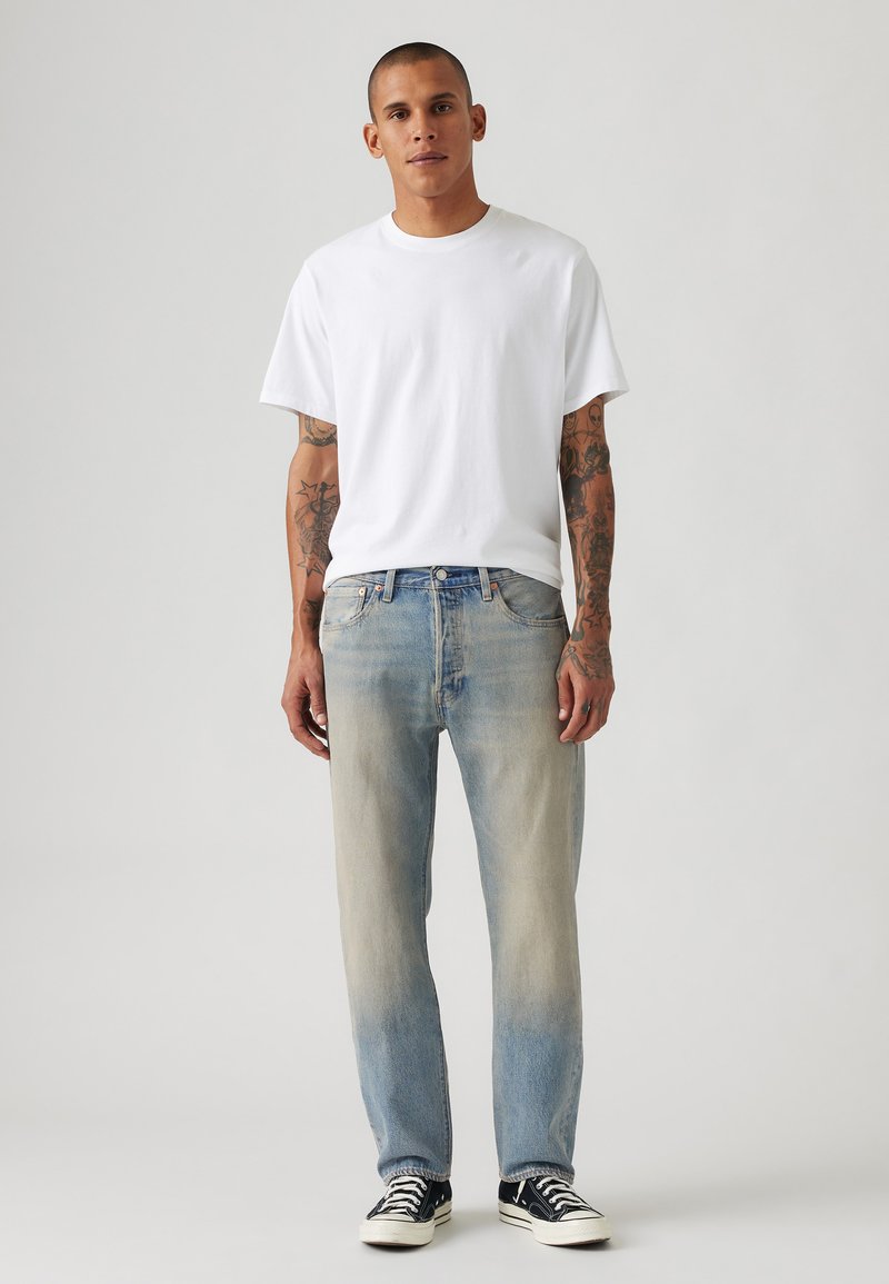 Weißes Baumwoll-T-Shirt, hellblaue, ausgewaschene Jeans und schwarze Sneaker mit weißen Sohlen. Einfacher, lässiger Schnitt mit einem entspannten Design.