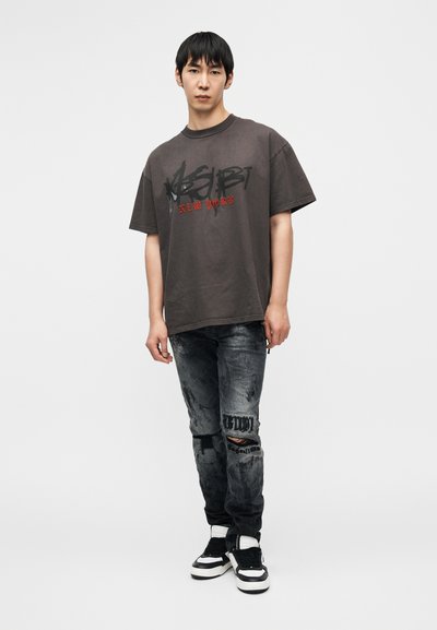 Υπερμεγέθη σκούρο γκρι μπλούζα με μαύρο και κόκκινο κείμενο. Συνδυάζεται με μαύρο φθαρμένο τζιν με σκισίματα και μαύρα και λευκά αθλητικά παπούτσια.