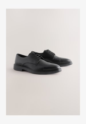 Zapatos de vestir de cuero negro con un acabado liso, punta redondeada y cordones. Presentan una suela plana de goma y detalles sutiles en la puntera.