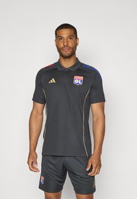 Donkergrijze sport polo met gouden accenten, voorzien van kleurrijke strepen in rood en blauw op de schouders, en een logo op de borst.