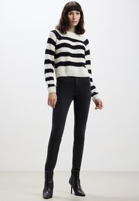 Maglione lavorato a maglia a strisce bianche e nere con texture a coste e scollatura rotonda, abbinato a jeans neri aderenti e stivaletti alla caviglia.