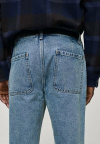 Svetlo modri denim usnjaki z ohlapnim krojem, ki imajo dve zadnji žepek in vidno šivanje. Material ima rahlo teksturirano površino.