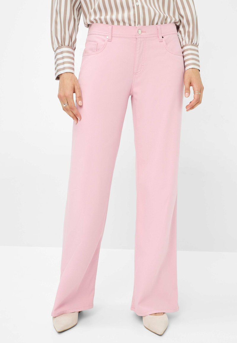 Jeans larges de couleur rose clair en tissu doux. Comprend cinq poches, une fermeture à bouton et des passants de ceinture. Associé à une chemise à rayures à manches longues.