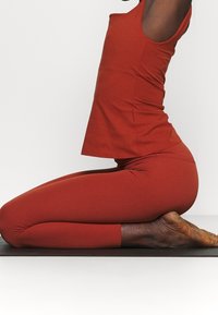 Il completo sportivo rosso include una maglietta senza maniche e leggings abbinati. Entrambi sono aderenti, con una texture liscia e senza motivi o accessori visibili.