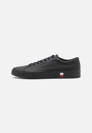 Low-top black sneaker with black laces, subtle side branding, and a small red, white, and blue striped detail near the sole.