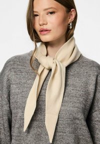Bufanda beige hecha de un tejido suave, atada en un nudo alrededor del cuello. Se lleva con un suéter gris texturizado, creando un look en capas.