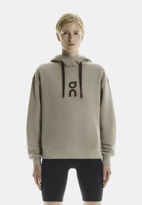 Hoodie beige chiaro con un grande logo nero sul fronte, caratterizzato da stringhe, una vestibilità comoda e polsini a coste, abbinato a pantaloni corti neri.