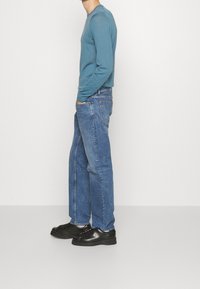 Camisa de manga larga azul claro, corte ajustado. Combinada con vaqueros de corte holgado y desgastados, y zapatos negros de cordones. Diseño simple y minimalista.
