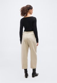 Γυναίκα με σγουρά μαλλιά σε αλογοουρά που φοράει μαύρο τοπ με μακριά μανίκια, μπεζ φαρδιά παντελόνια cropped και μαύρα μποτάκια με τακούνι, με την πλάτη προς τον φακό.