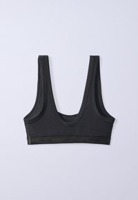 Μαύρο αθλητικό σουτιέν Calvin Klein με φαρδιές τιράντες και λαστιχένιο λογότυπο, τοποθετημένο επίπεδο σε ανοιχτό γκρι φόντο.