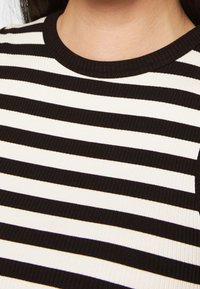 Maglia a righe bianco e nero in punto costina con scollatura a girocollo. Il tessuto ha una finitura текстurizzata, caratterizzata da righe orizzontali di diverse larghezze.