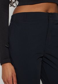 Czarne materiałowe spodnie o gładkiej fakturze, z kieszenią na zamek, regulowanym sznurkiem i dopasowanym krojem w talii.