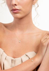 Gouden kettingjuwelen met een kleine heldere gemstone hanger aan een ketting, vergezeld van een bijpassende armband en ring.