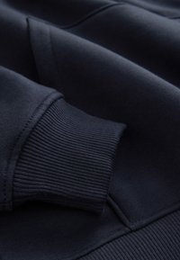 Gros plan d'une manche de sweat bleu marine montrant un bord-côtes et une texture de tissu douce.