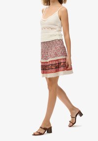 Top de punto blanco sin mangas con tirantes finos, combinado con una falda mini de múltiples patrones que presenta acentos florales, rosas y negros, y sandalias de tacón marrones.