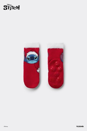 Chaussettes rouges avec un personnage de Stitch imprimé portant un chapeau de Père Noël. Poignets blancs duveteux et motifs de flocons de neige texturés sur les semelles.