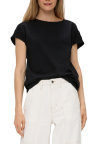 Czarna bawełniana koszulka z krótkimi, podwiniętymi rękawami oraz teksturowanym karczkiem, zestawiona z jasnymi spodniami o wysokim stanie z widocznymi szwami.